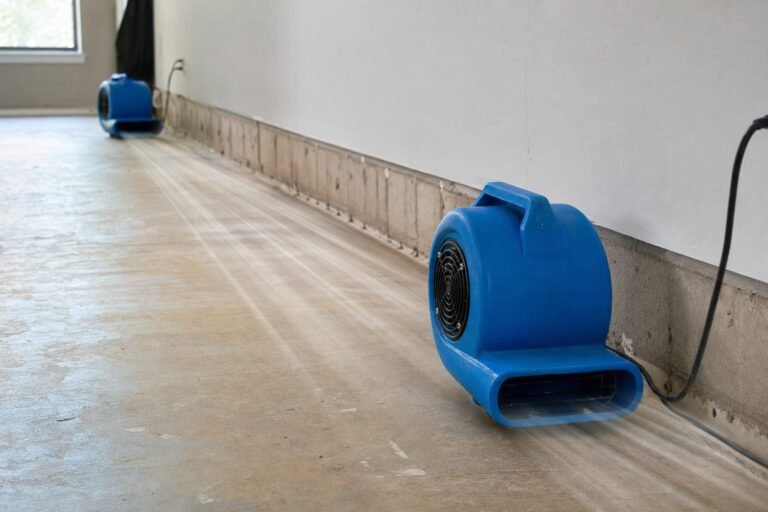Low-profile air mover directing airflow along a wall base and up the wall surface